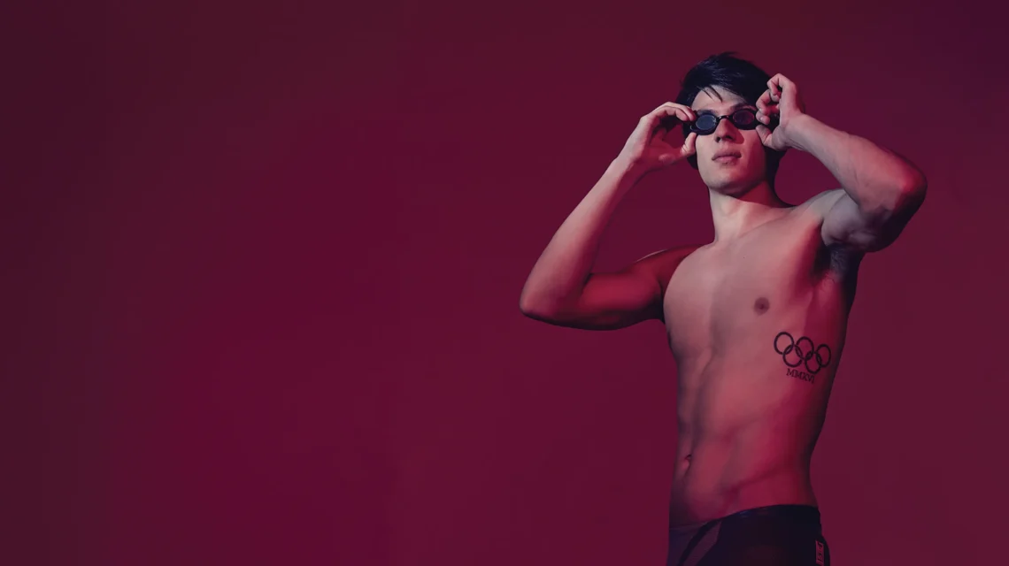 Photo of Joe Choong on a burgundy backdrop taking his swimming goggles off