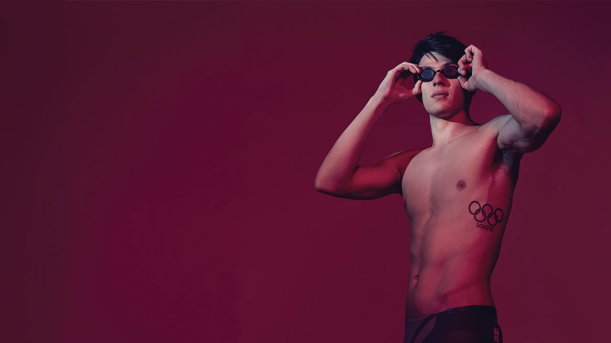 Photo of Joe Choong on a burgundy backdrop taking his swimming goggles off