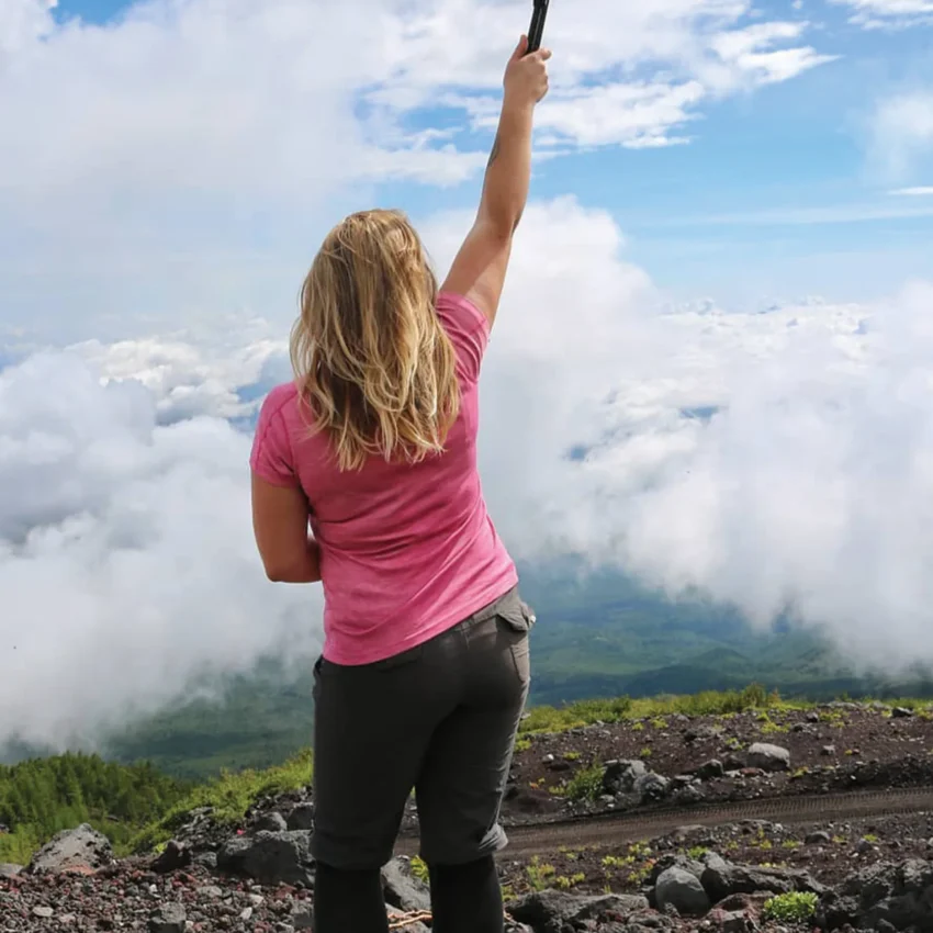 A women standing on mount fuji with a walking stick raised in the air