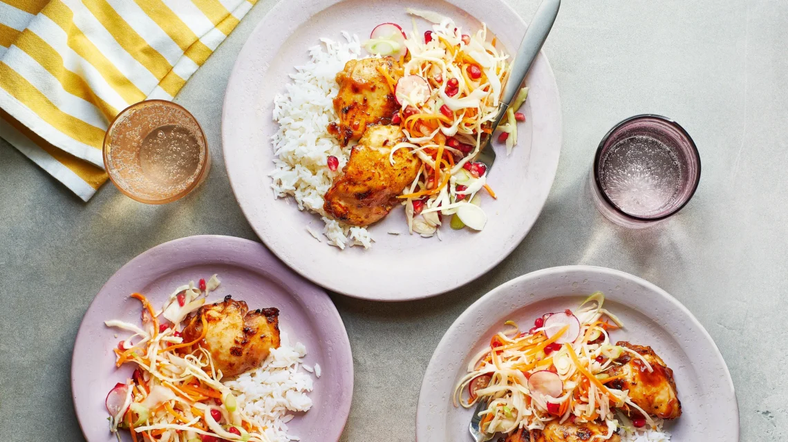 Three plates of grilled chicken on rice with vegetable slaw, accompanied by two glasses, on a light surface next to a yellow-striped cloth.
