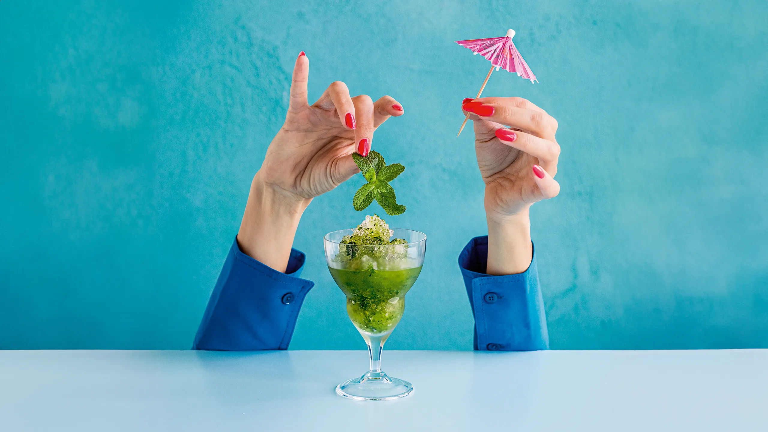 A green ice drink with two hands putting a umbrella into the top