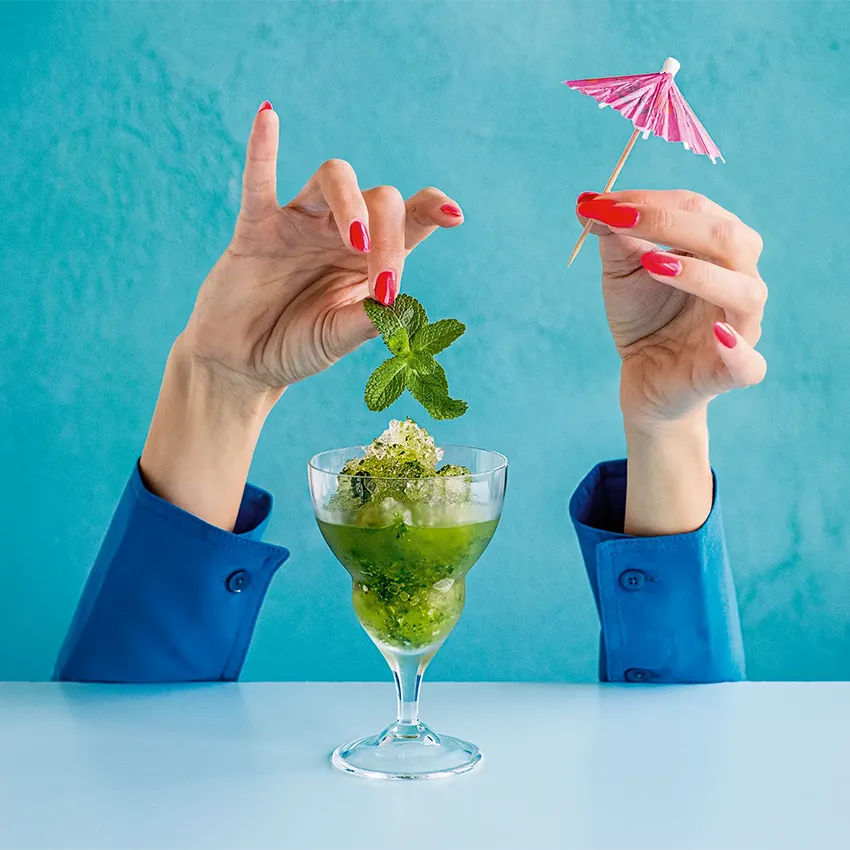 A green ice drink with two hands putting a umbrella into the top