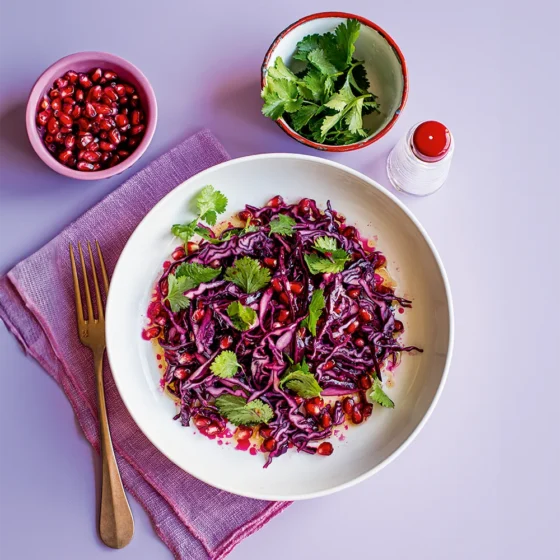 Purple cabbage salad with pomegranate and cilantro on a lavender surface.