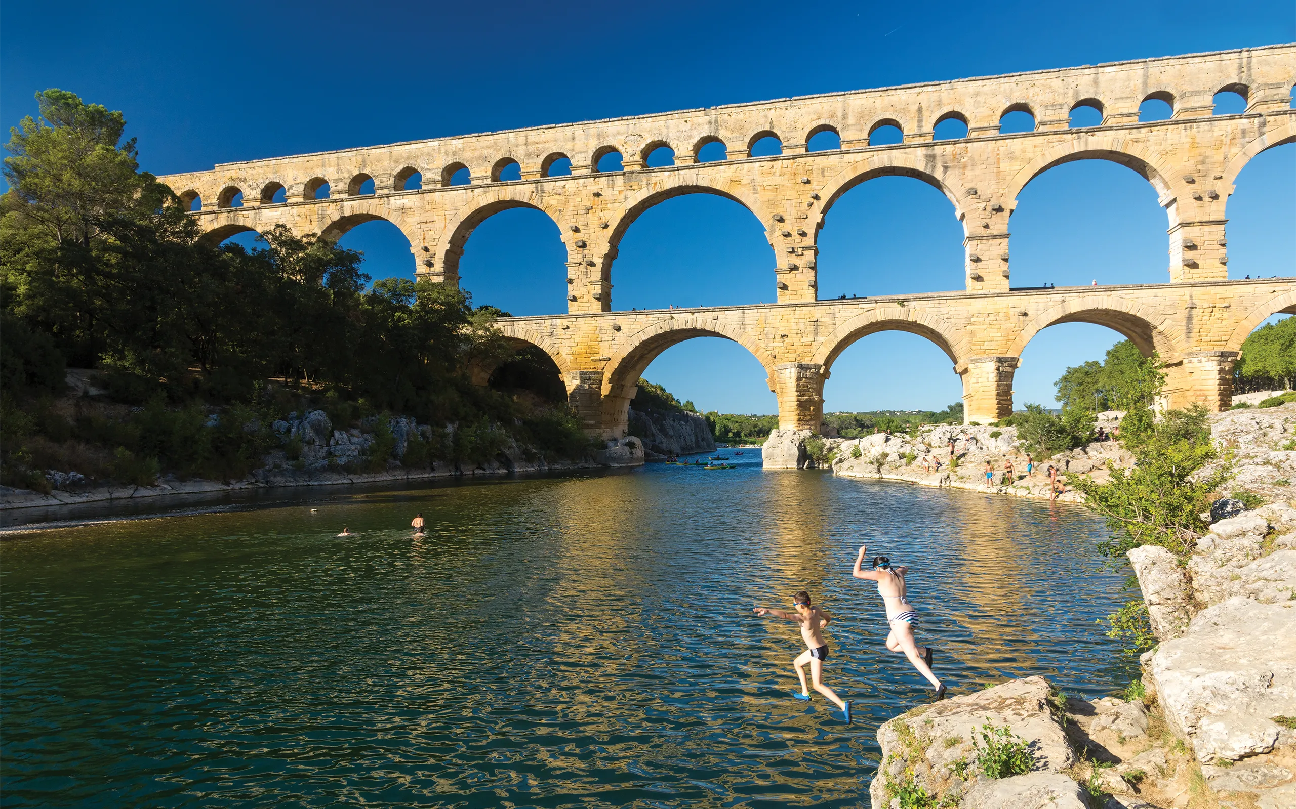 Couple jump into Gardon river with aquaduct in the background