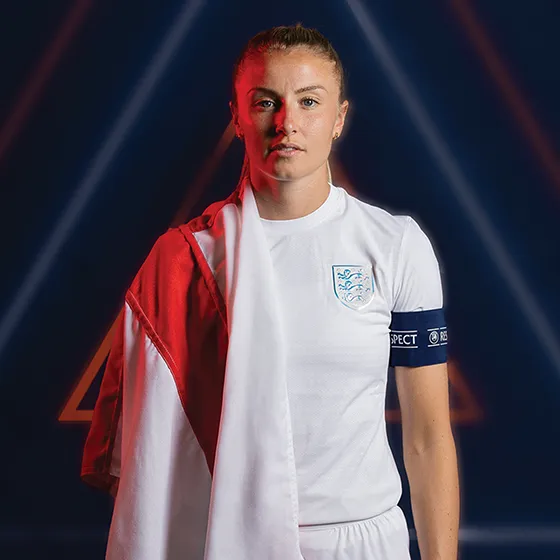 Picture of Leah Williamson wearing her England football kit with a England flag draped over her right shoulder