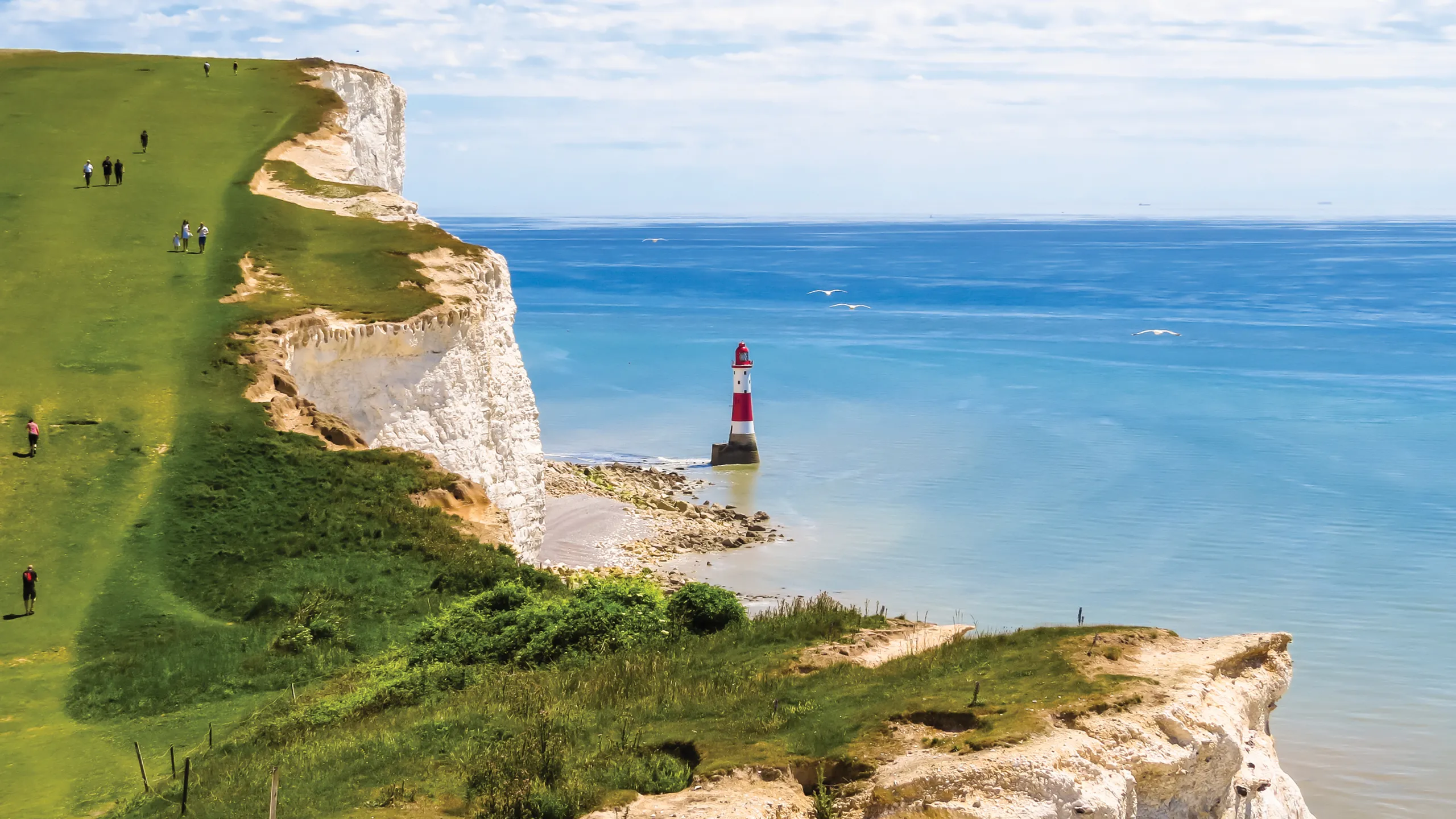coastline view of the sea with people walking along the cliff and a view of a lighthouse