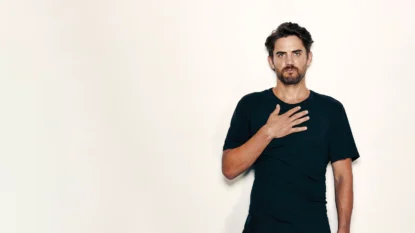 Portrait of Stuart Sanderman on a light backdrop with his hand on his heart area