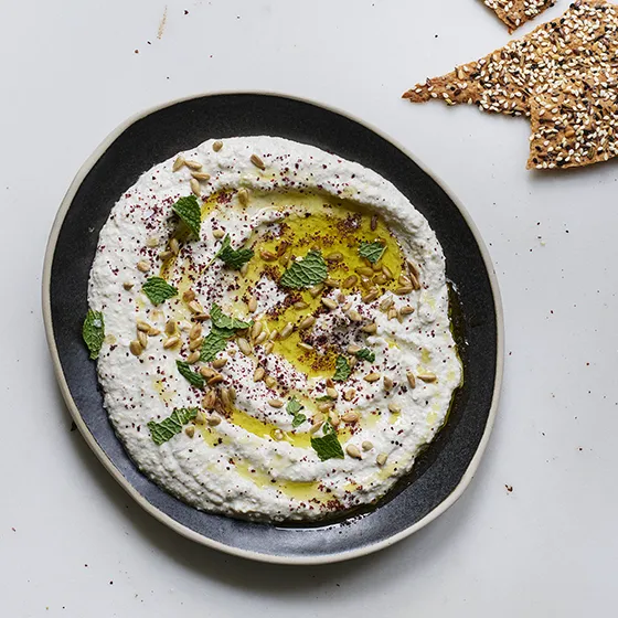 Creamy labneh topped with olive oil, sunflower seeds, and fresh mint, served on a dark plate with seeded crackers.