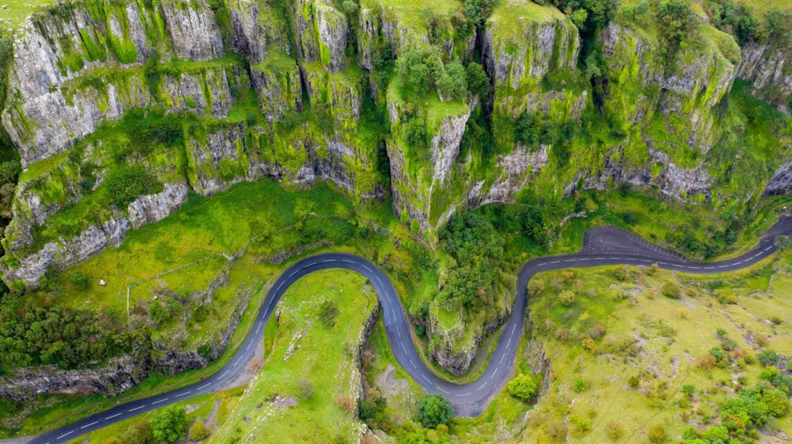 Aerial view of a winding road snaking through the steep, moss-covered limestone cliffs of Cheddar Gorge.