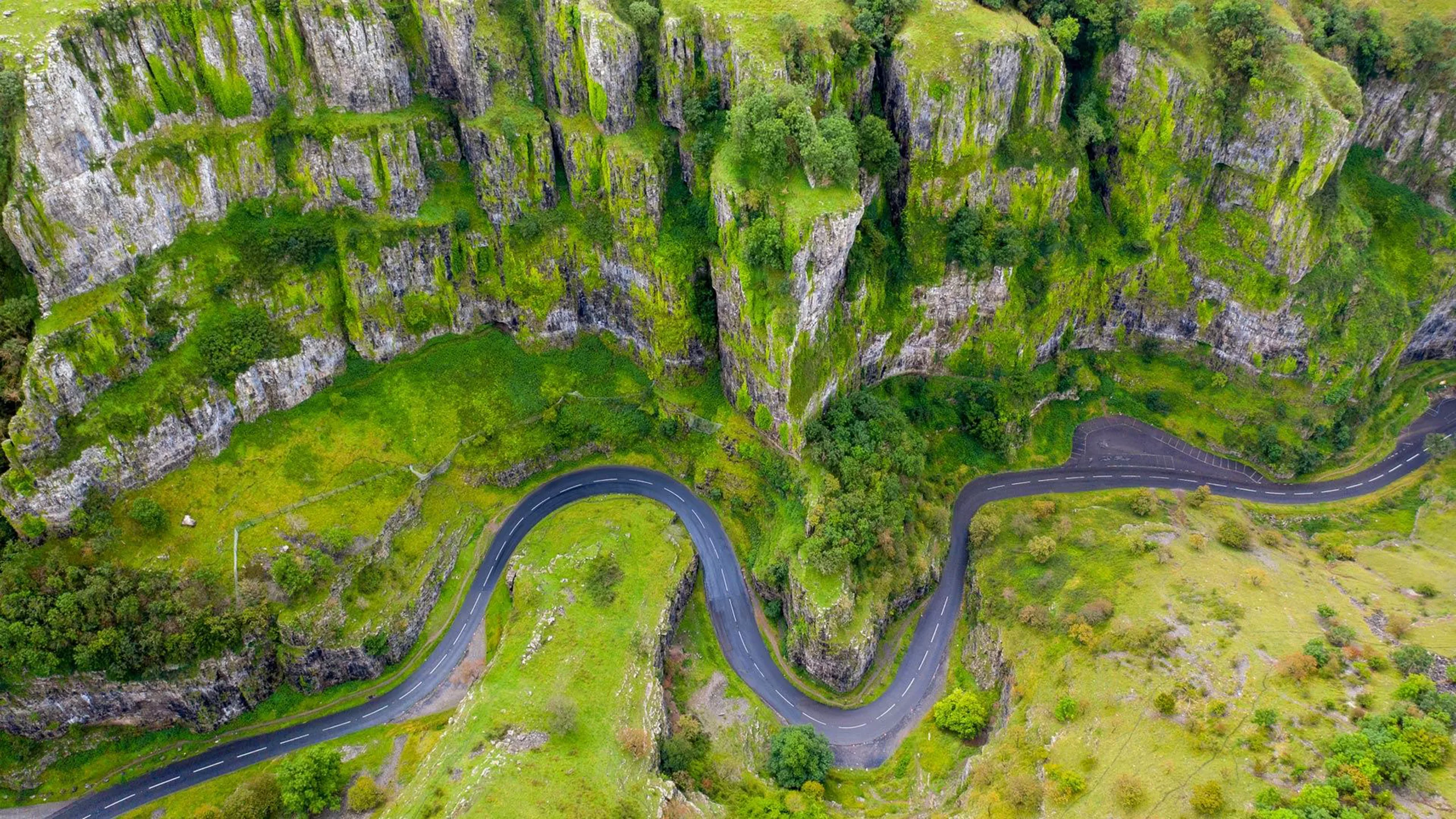 Aerial view of a winding road snaking through the steep, moss-covered limestone cliffs of Cheddar Gorge.