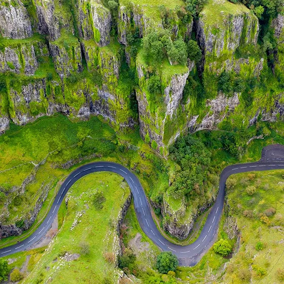Aerial view of a winding road snaking through the steep, moss-covered limestone cliffs of Cheddar Gorge.