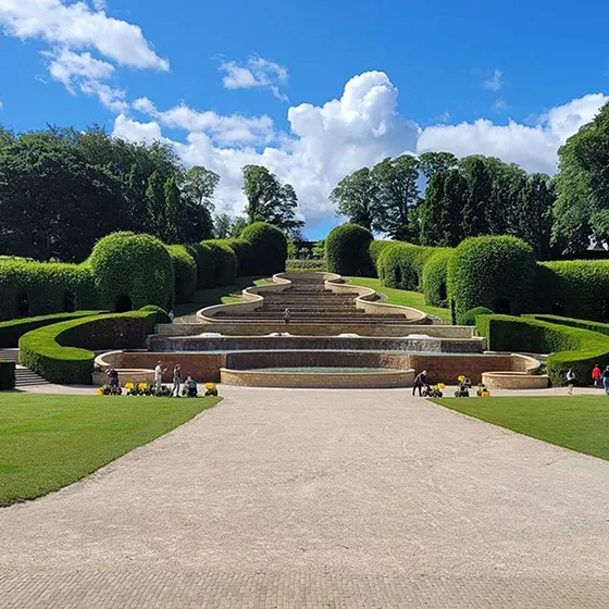 The Grand Cascade at The Alnwick Garden features tiered water fountains framed by sculpted hedges and a wide gravel path.