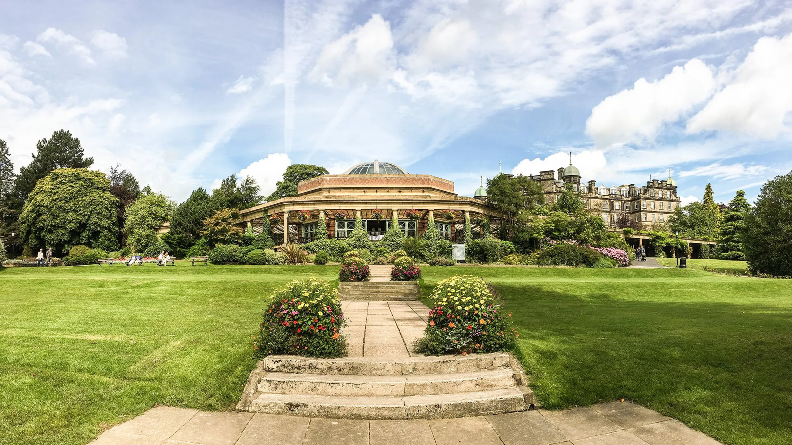 Stone steps and a paved path lead through a manicured lawn toward the Sun Pavilion in Harrogate's Valley Gardens.